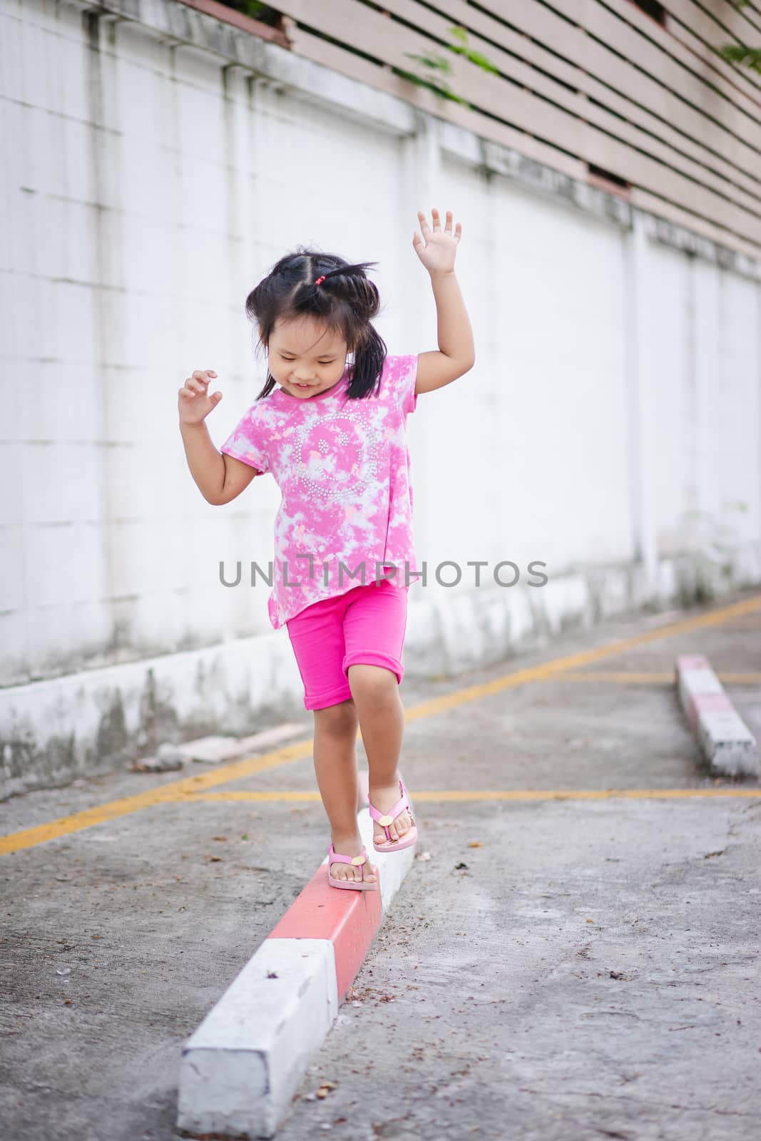 Little asian girl walking on the curb and trying to keep her balance