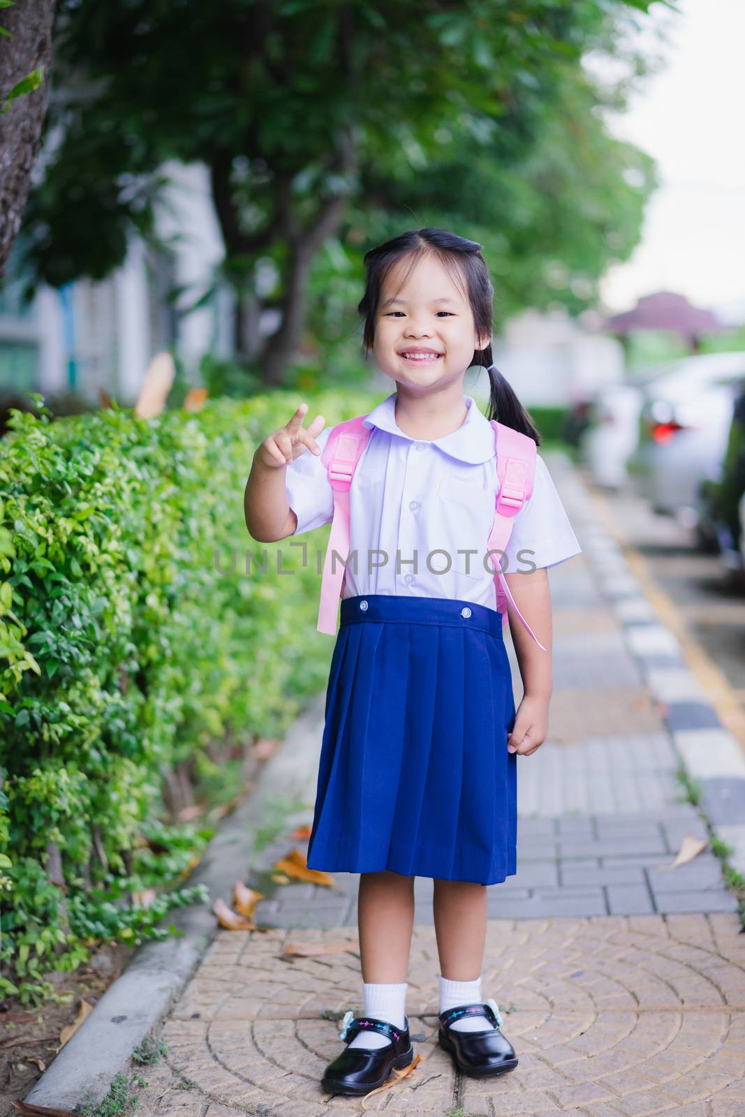 happy little girl in Thai school uniform with backpack standing by domonite