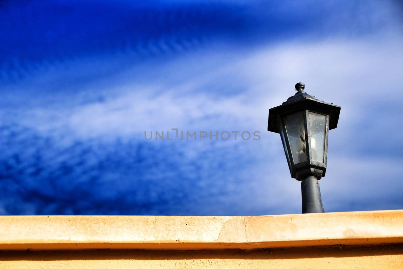 Black Lamppost on wall under cloudy blue sky