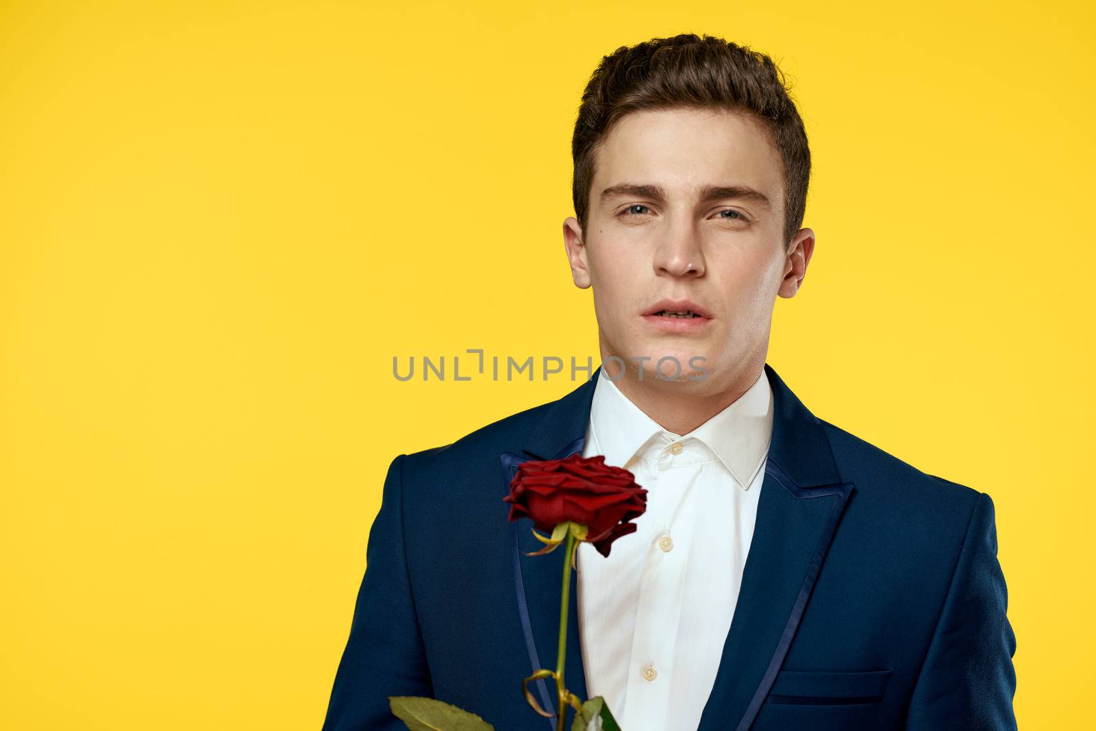 Young man in a classic suit with a red rose in his hand on a yellow background emotions cropped view model. High quality photo