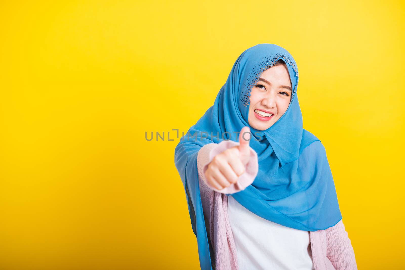 Asian Muslim Arab, Portrait of happy beautiful young woman Islam religious wear veil hijab funny smile she made finger thumbs up, Ok sign to agree, studio shot isolated on yellow background