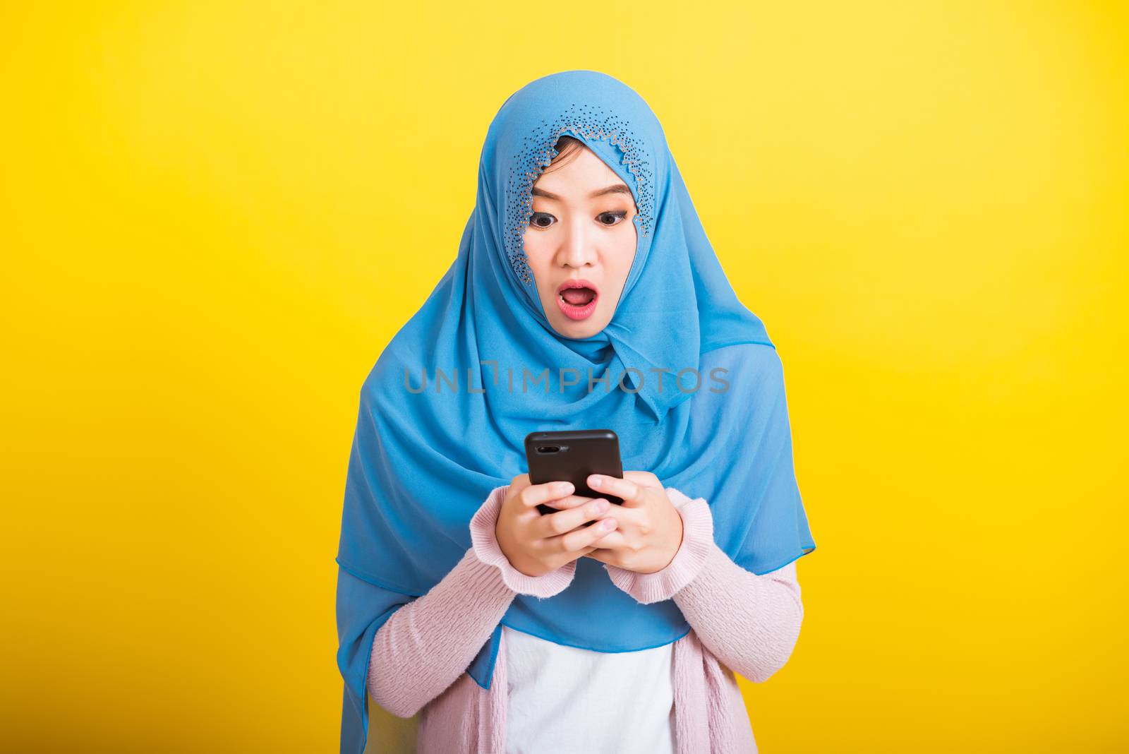 Asian Muslim Arab, Portrait of happy beautiful young woman Islam religious wear veil hijab funny smile she reads surprised confused shock news open mouth, studio shot isolated on yellow background
