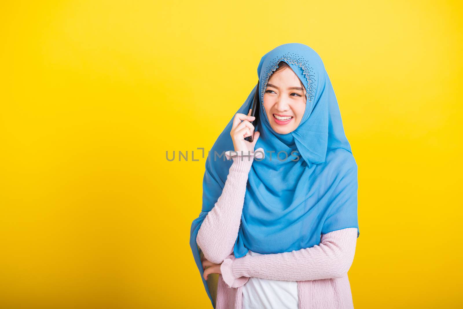 Asian Muslim Arab, Portrait of happy beautiful young woman Islam religious wear veil hijab funny smile she talking on mobile smart phone against, studio shot isolated on yellow background
