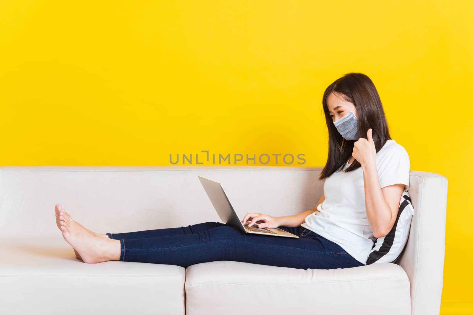Woman sitting on sofa wearing face mask protective she work from by Sorapop