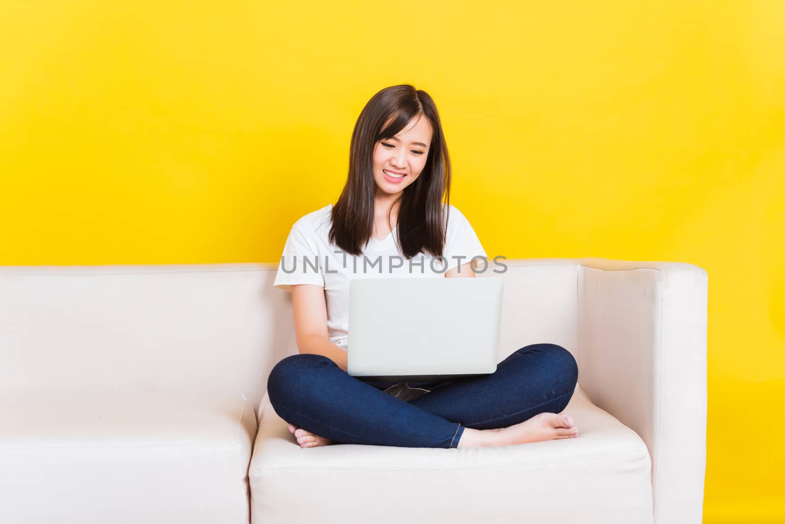 Portrait Asian of happy beautiful young woman work from home she sitting on sofa using laptop computer in house living room studio shot isolated on yellow background