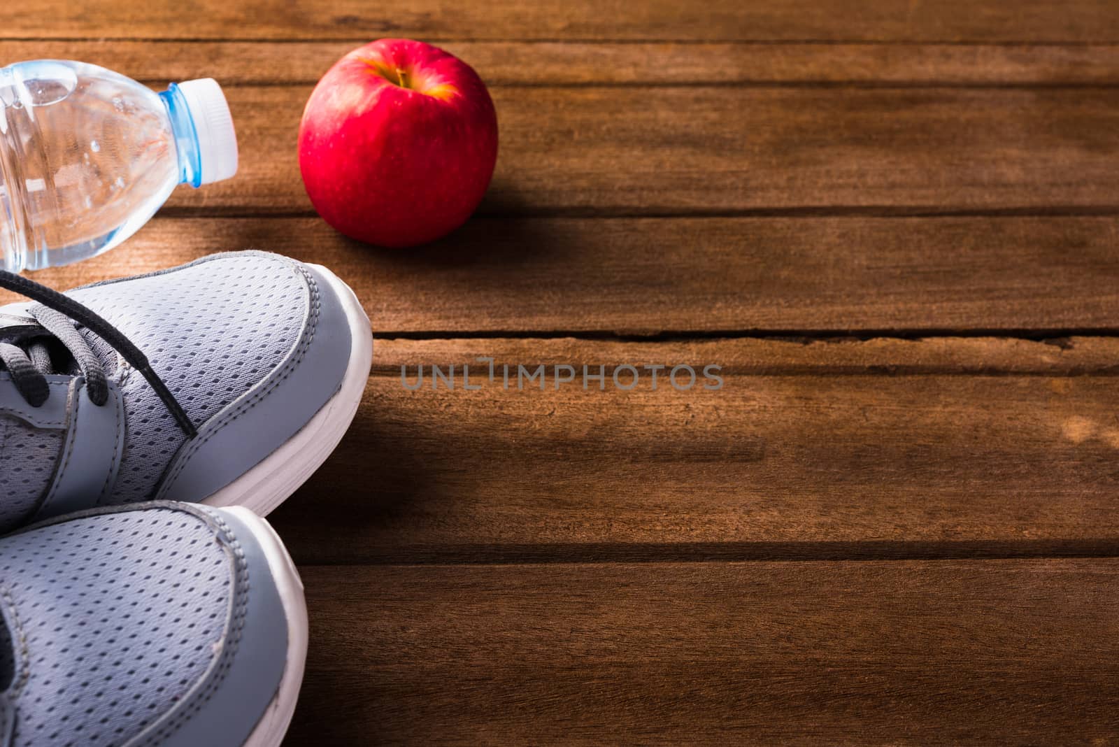 pair sports shoes, bottle water and red apple on wood table by Sorapop