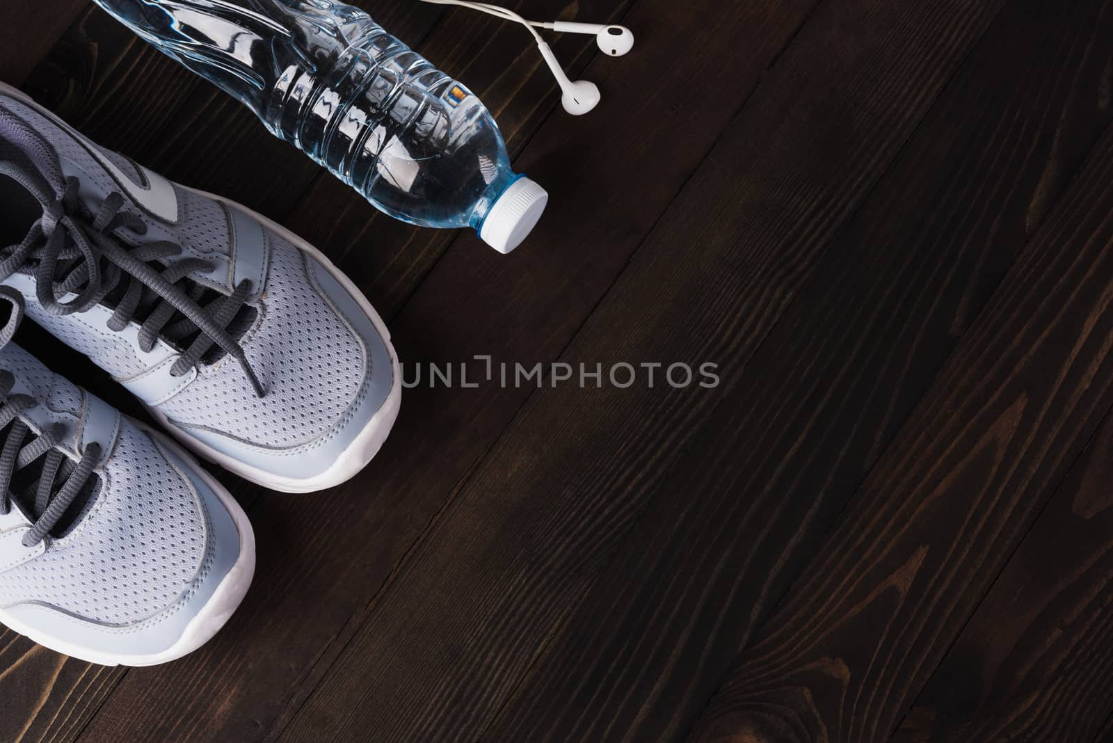 pair sports shoes, headphones and water bottle on black wood by Sorapop
