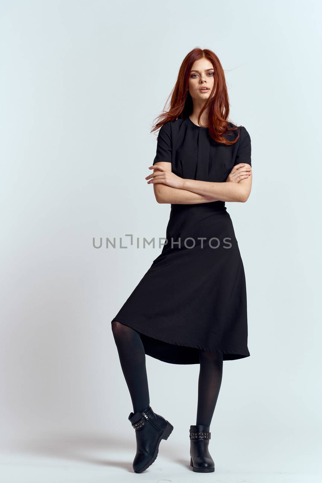 A woman in a black dress on a light background and pantyhose shoes red hair and pose in full growth. High quality photo