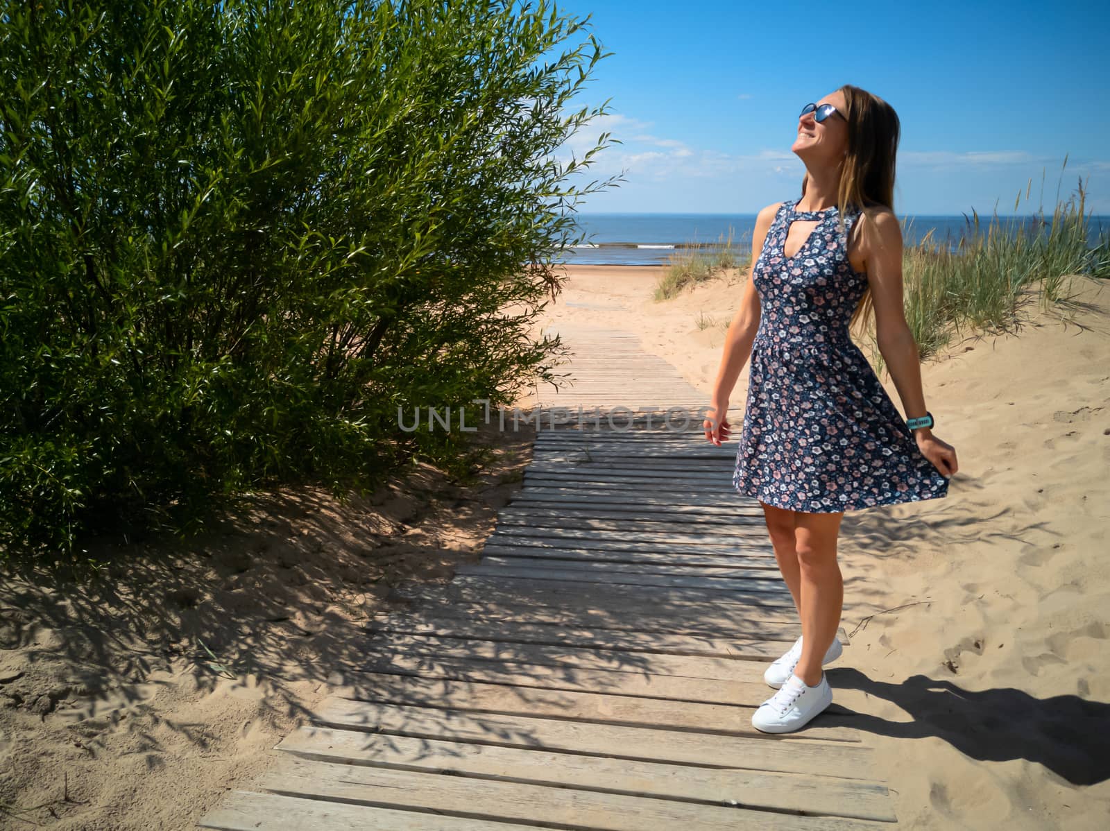 beautiful smiling girl alone on the beach. wooden path, blue sky and ocean background. Young woman in dress