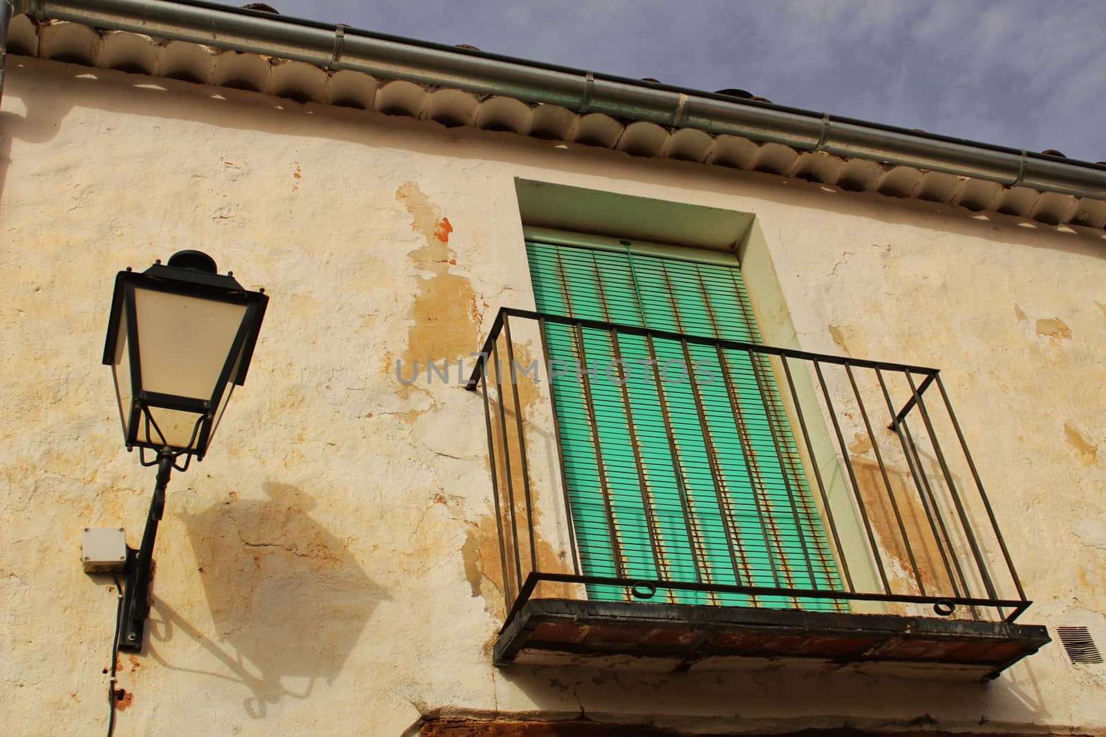 Old house facade with rusty balcony and green blind next to vintage streetlight. Alcaraz village, Castilla La Mancha, Spain.