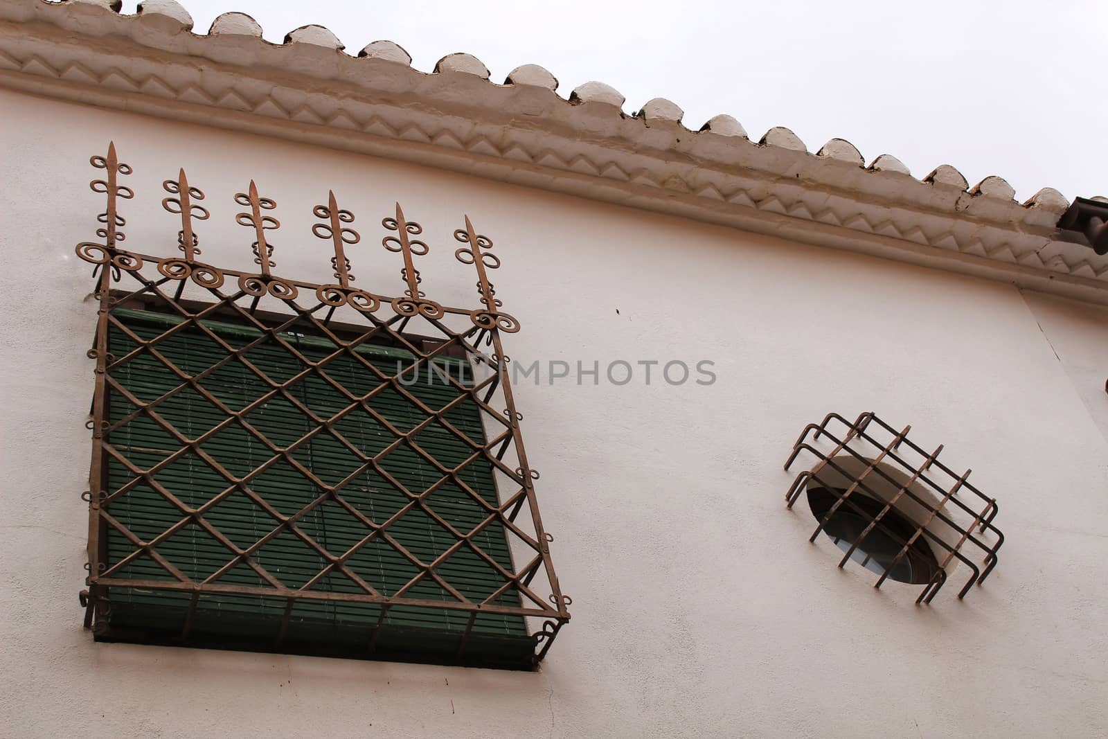 Window with wrought iron details and green blind on white stone facade in Villanueva de los Infantes, Castile-la Mancha, Spain