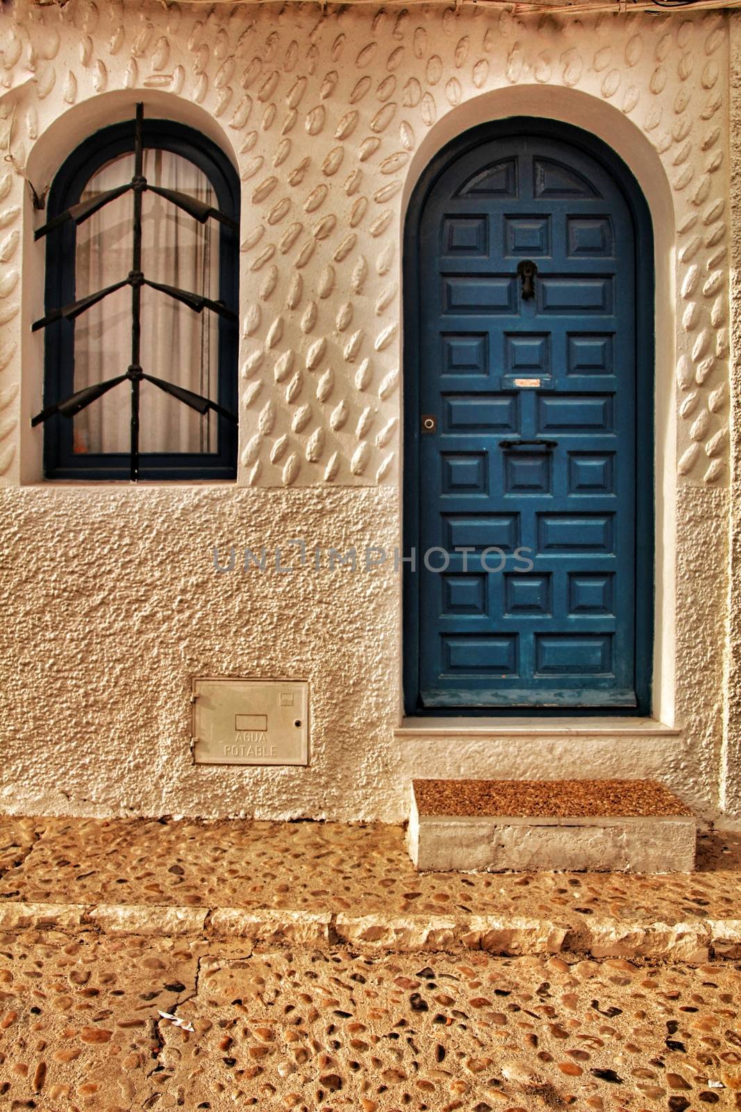 Blue door and white facade with iron details in Altea, Alicante, Spain. Cobbled floor in the street.