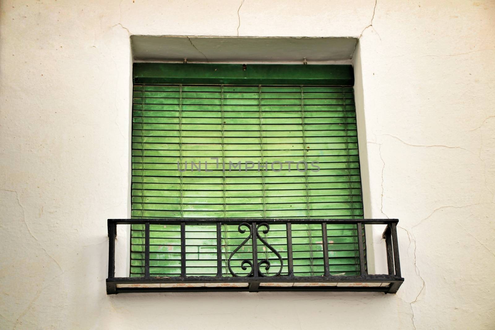 Old house facade with rusty balcony and green blind in Cordoba, Spain.
