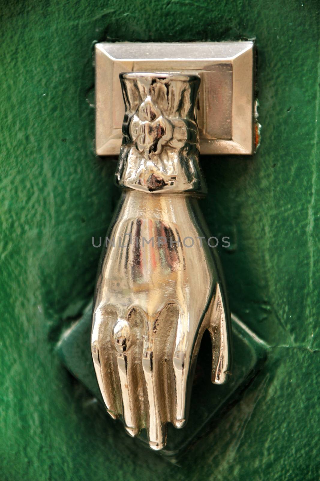 Door knocker with hand shape on green wooden door