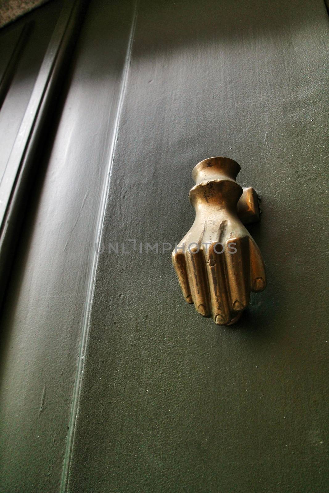 Golden doorknocker with hand shape on old green wooden door in Porto, Portugal