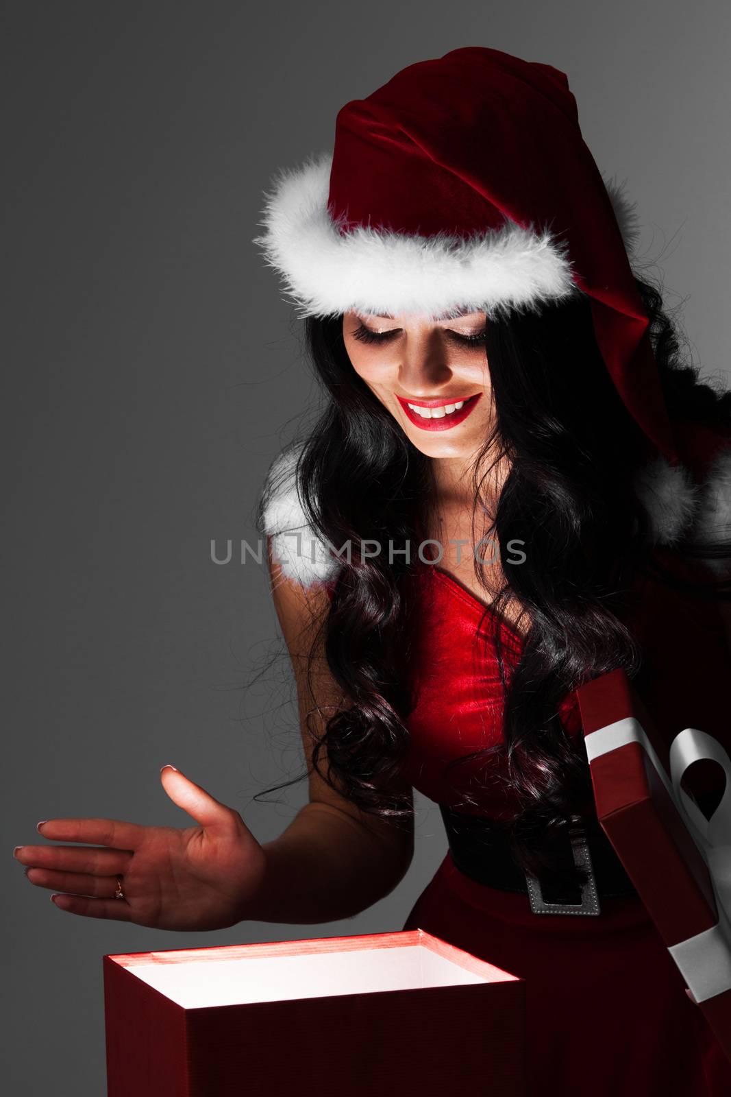 Beautiful santa girl opening glowing magic gift and smiling