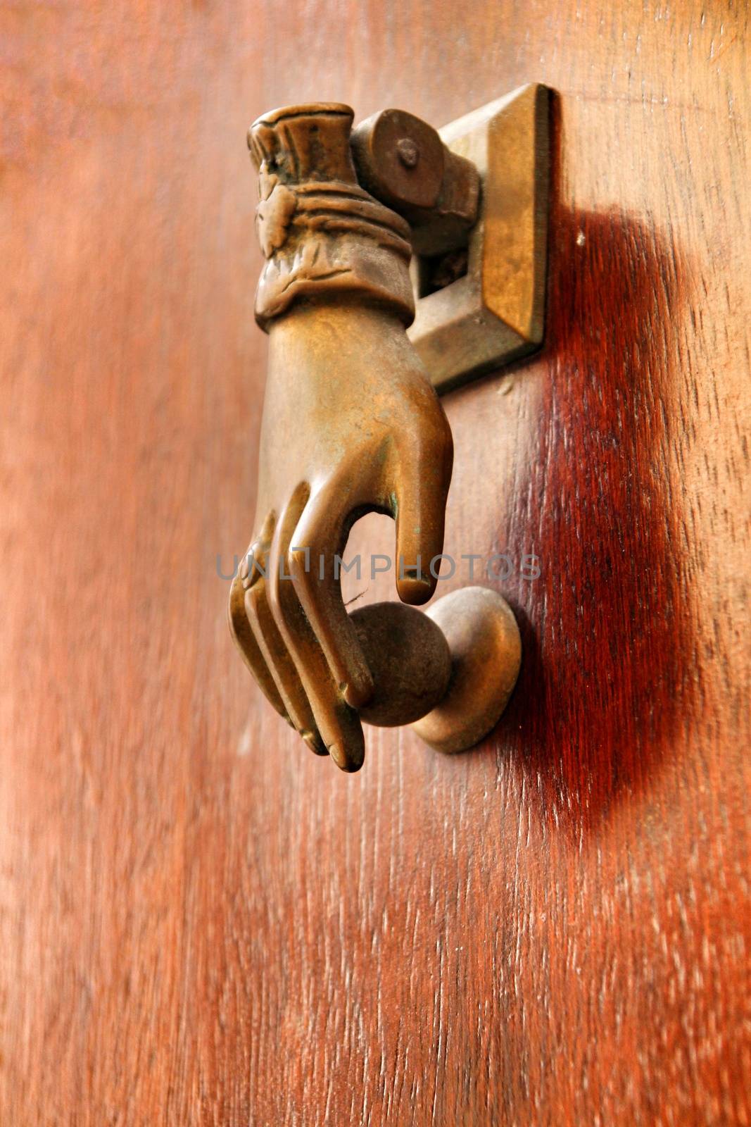 Golden doorknocker with hand shape on old wooden door by soniabonet