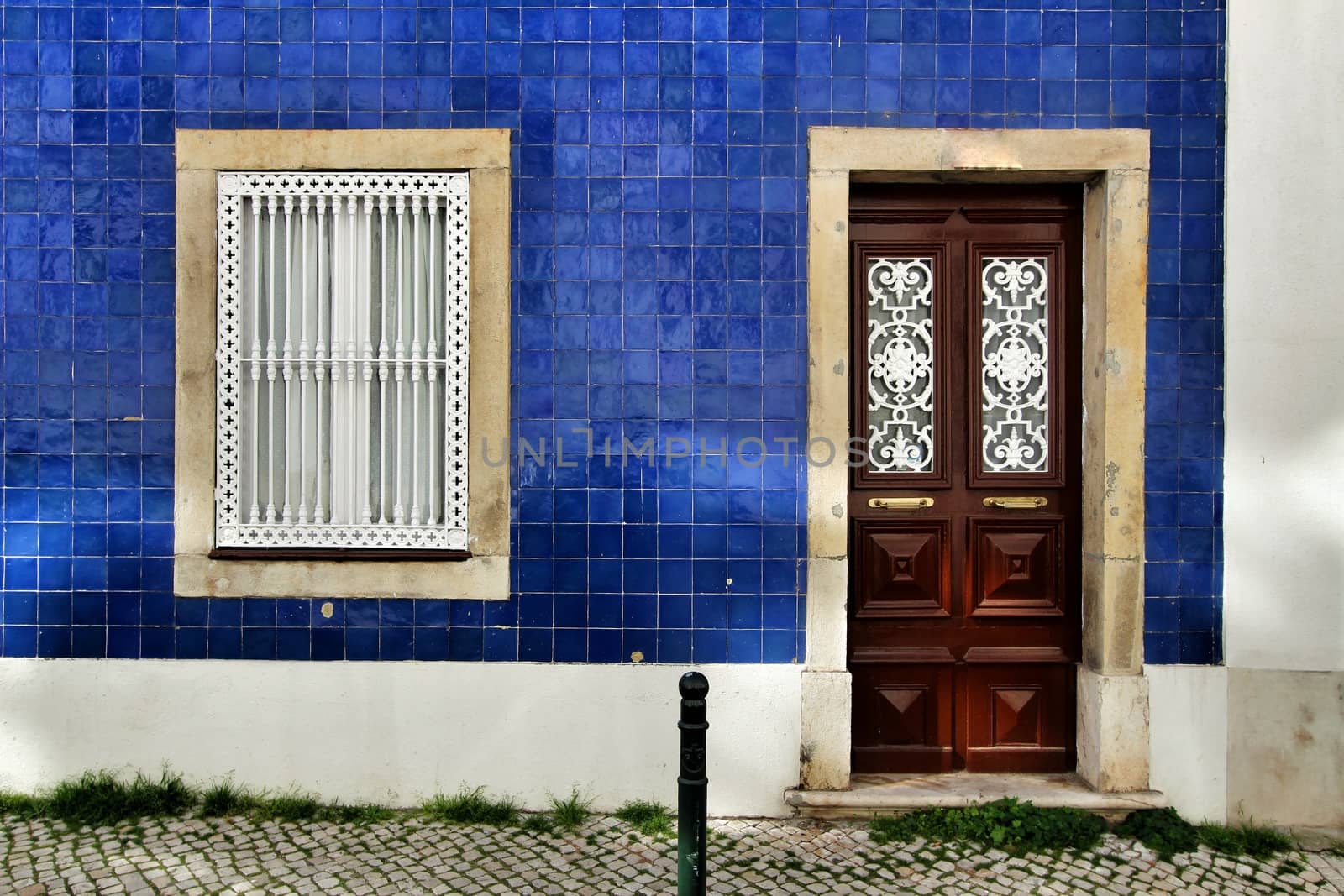 Old and colorful wooden door with iron details and blue tiled facade in Lisbon, Portugal