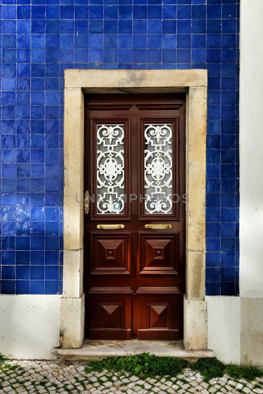 Old and colorful wooden door with iron details and blue tiled facade in Lisbon, Portugal