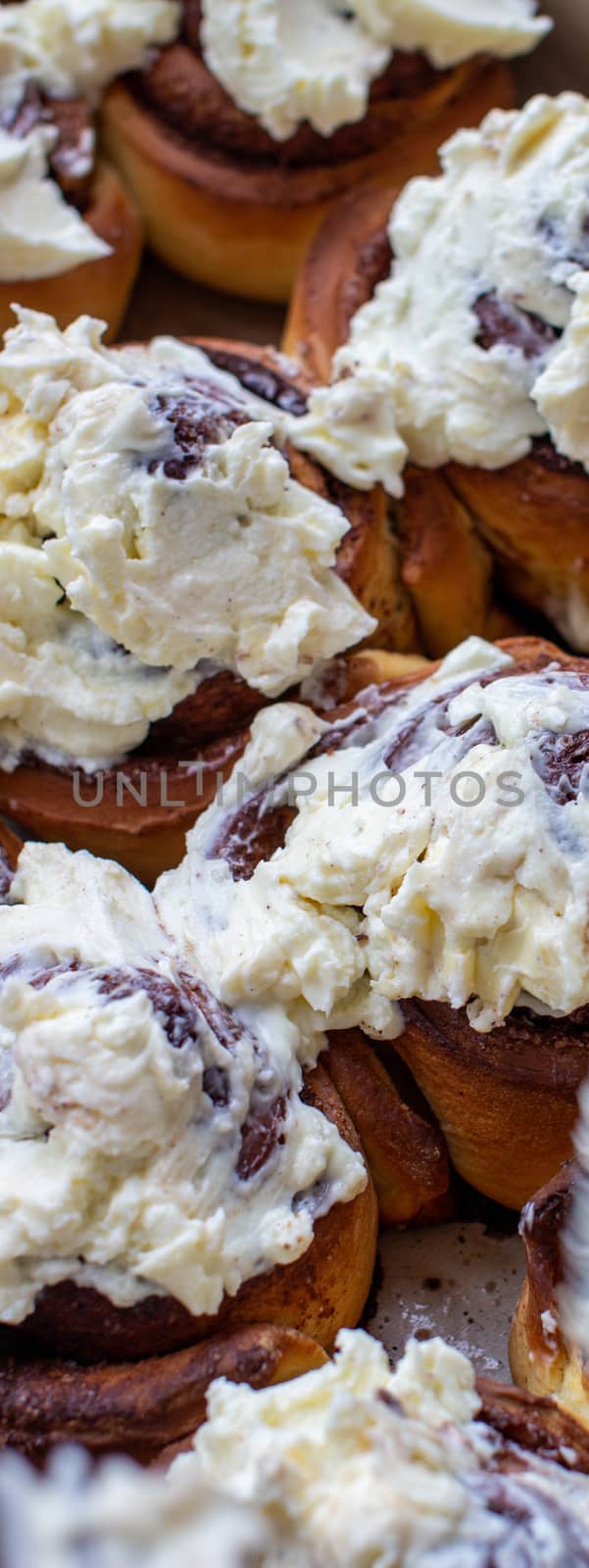 Delicious round rolls of dough with cinnamon on top smeared with sweet cream on a baking sheet after the oven. I cook buns at home in the oven.