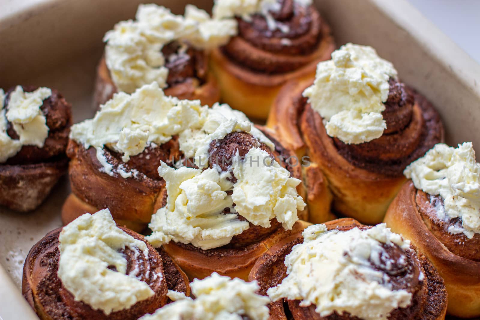 Delicious round rolls of dough with cinnamon on top smeared with sweet cream on a baking sheet after the oven. I cook buns at home in the oven.