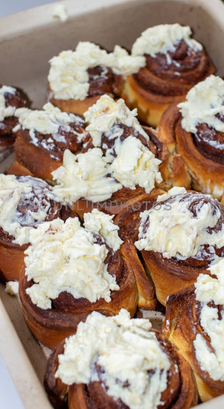 Delicious round rolls of dough with cinnamon on top smeared with sweet cream on a baking sheet after the oven. I cook buns at home in the oven.