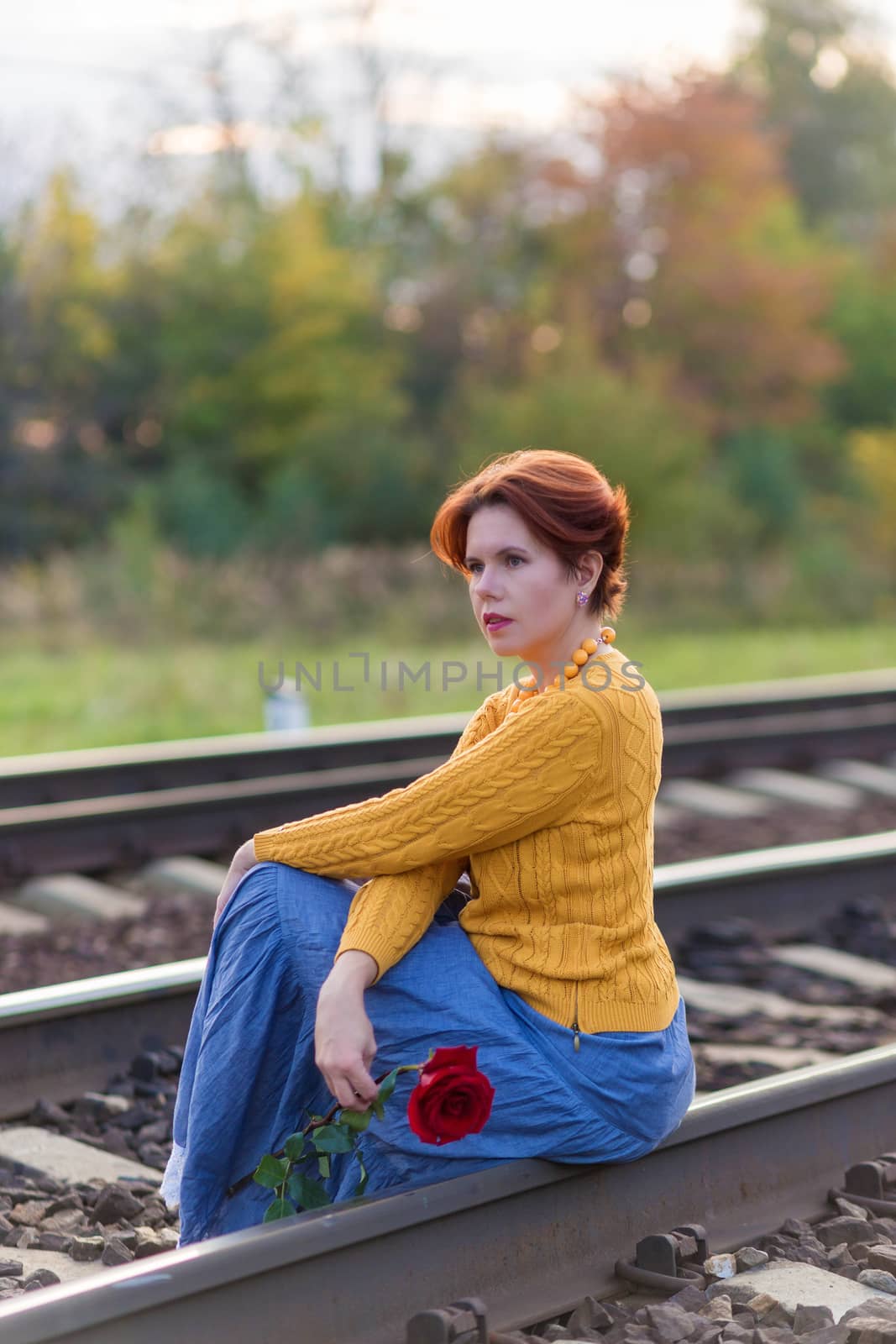 The woman sitting on rails of the railway holding red rose