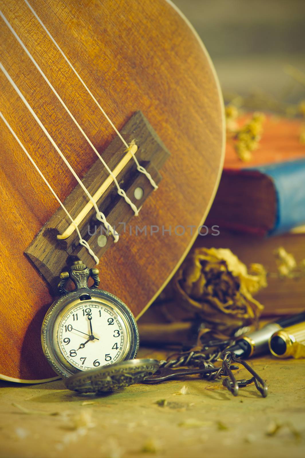 An antique pocket watch leaned against a ukulele and old book with vintage map and brass pen placed on wooden table. closeup and copy space for text. The concept of memories or things in the past.