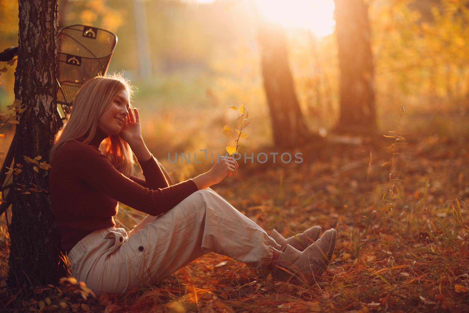 young woman sitting near tree with vintage bicycle in autumn park at sunset by primipil