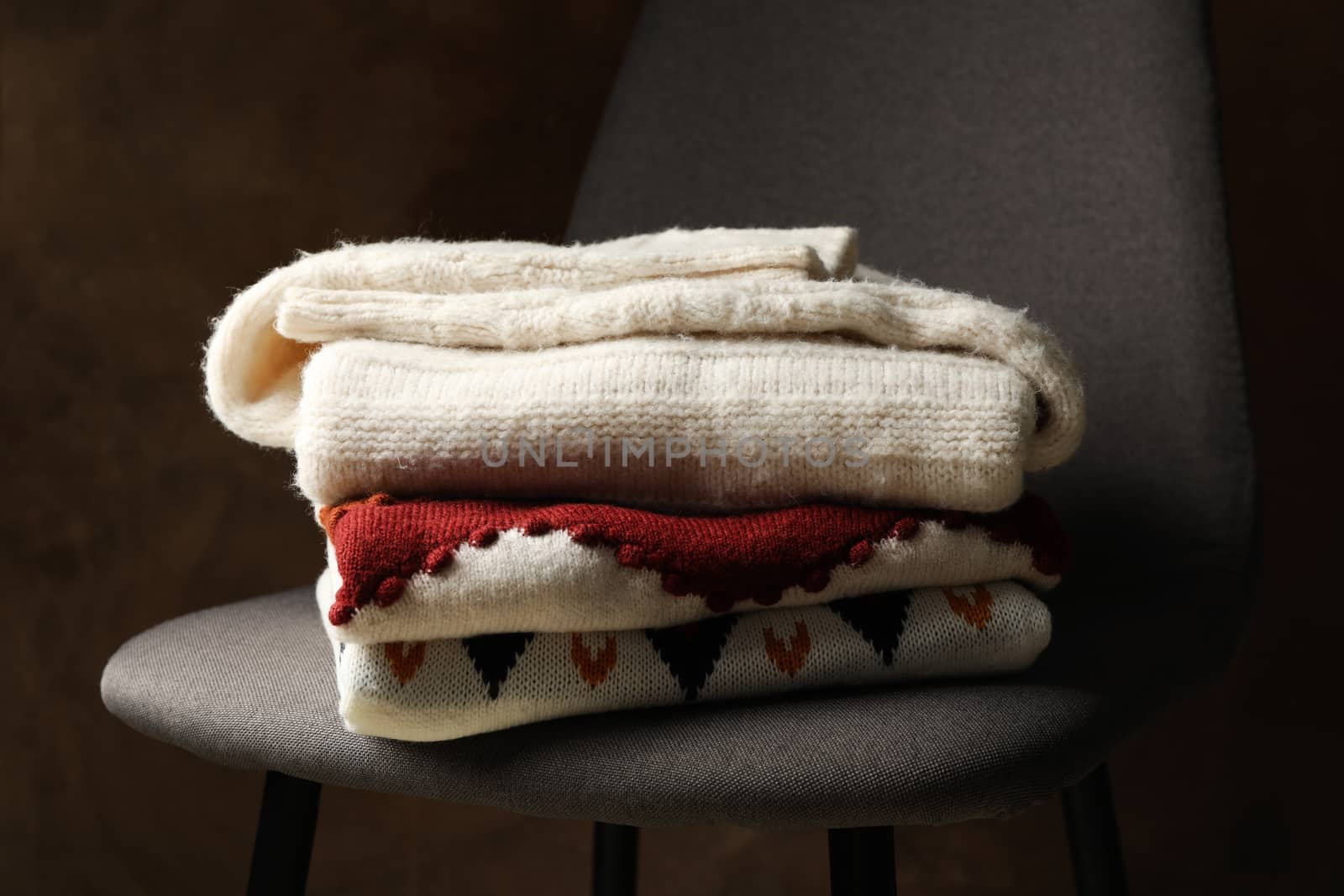 Pile of sweaters on chair against brown background by AtlasCompany