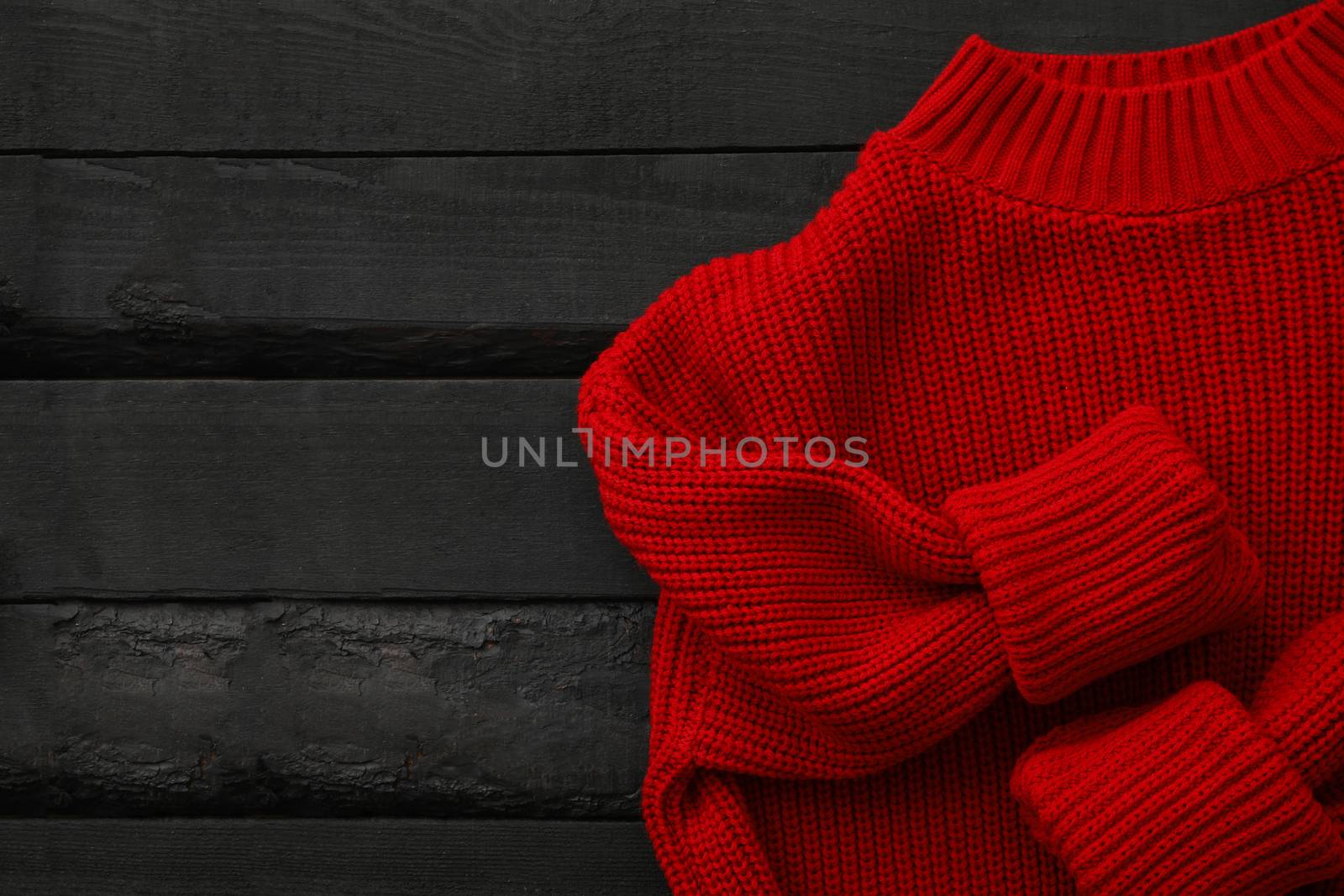 Red knitted sweater on wooden background, top view