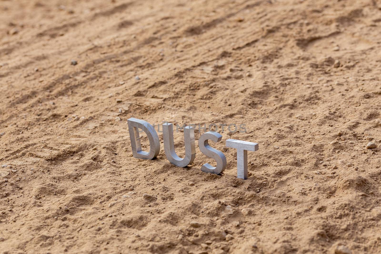 the word dust standing on dusty road surface in linear perspective with selective focus and background blur under direct sunlight