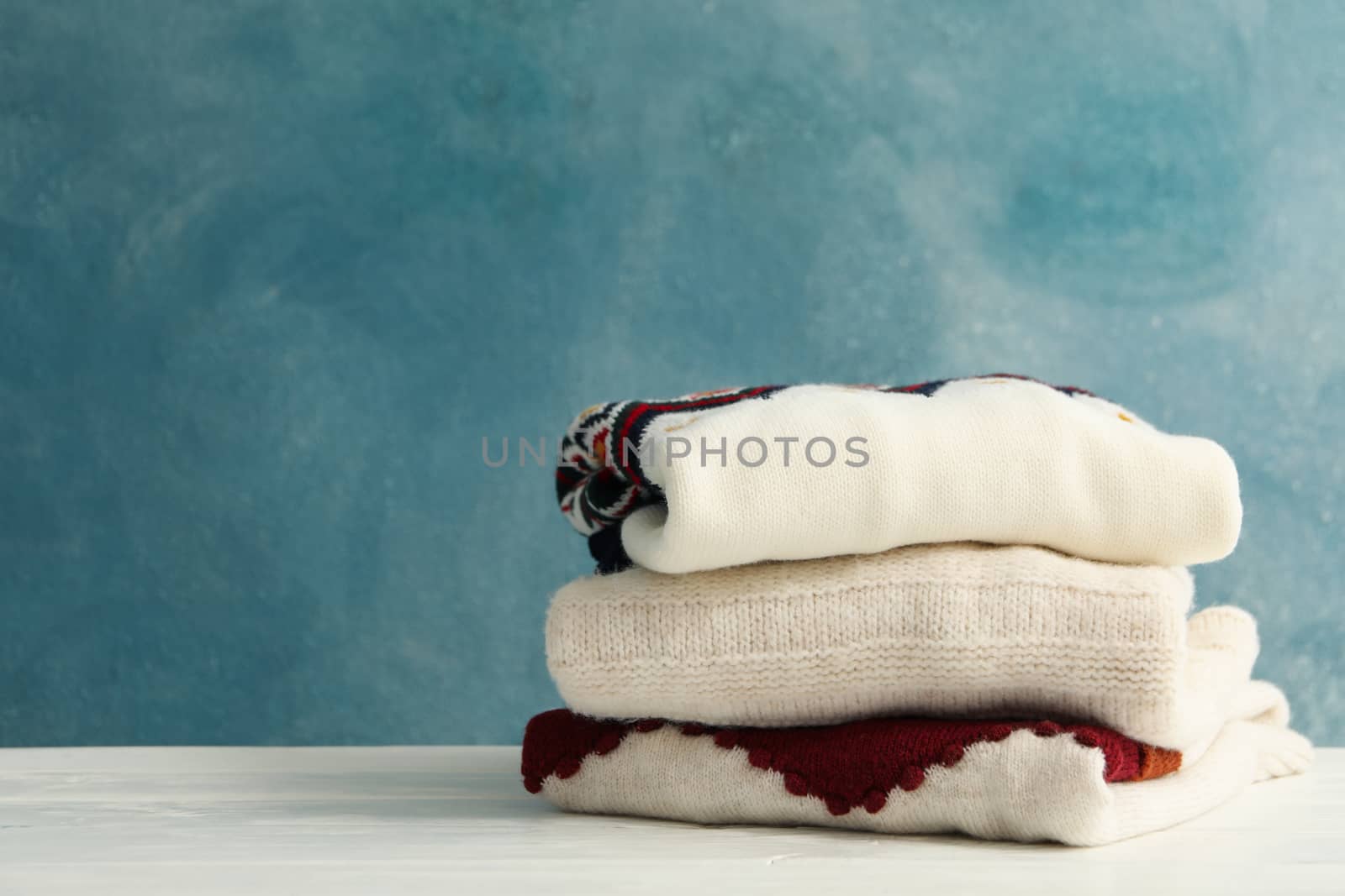 Pile of sweaters on white wooden table against blue background