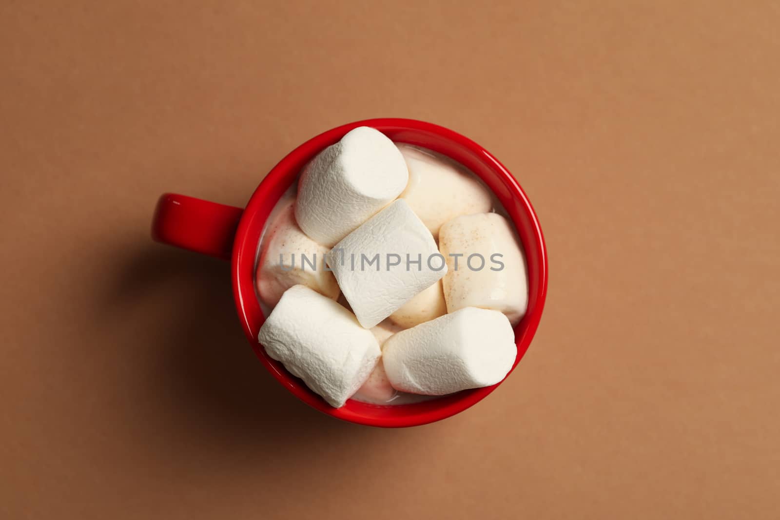 Cup with marshmallows on brown background, top view