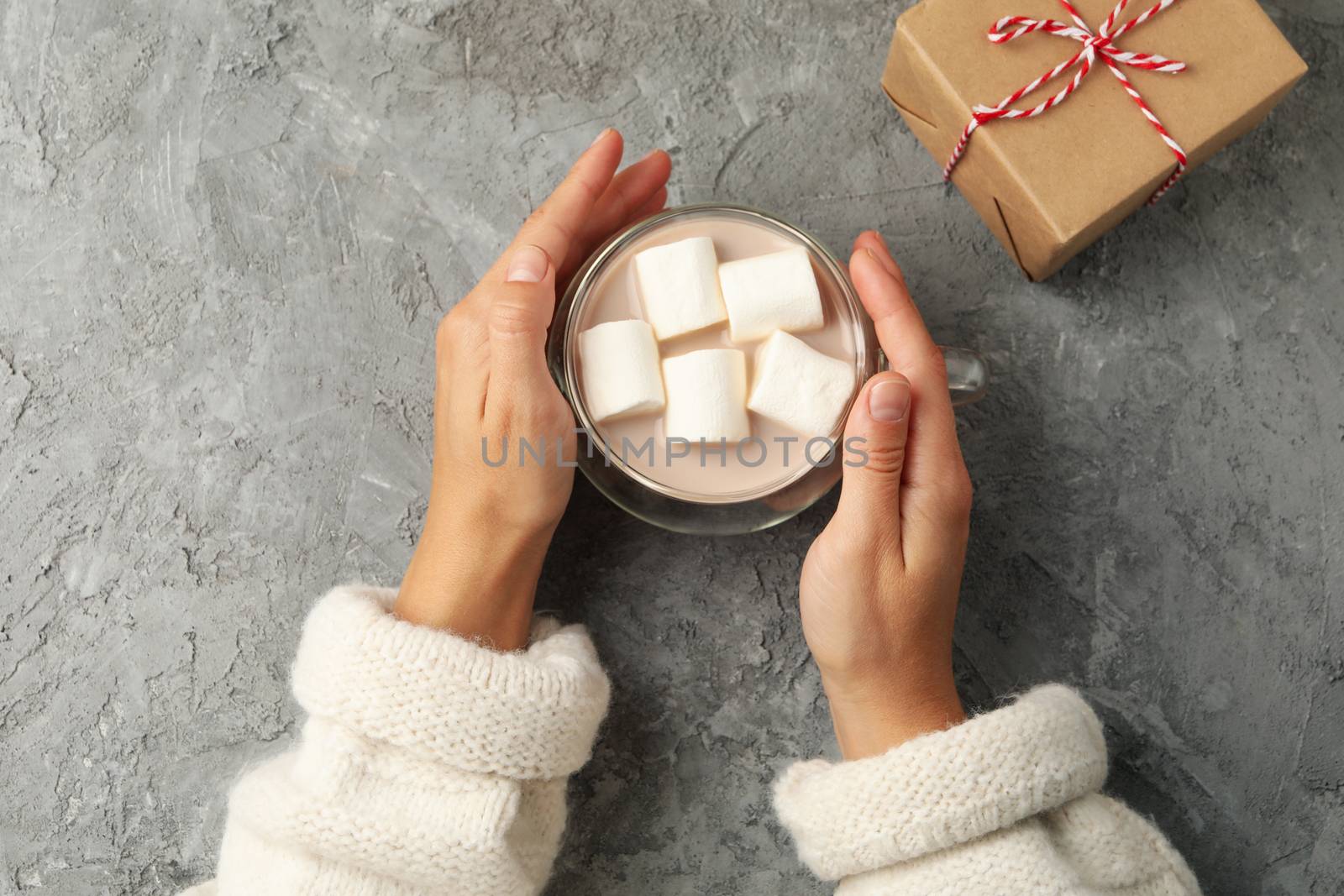 Female hands hold cup of coffee with marshmallows on gray backgr by AtlasCompany