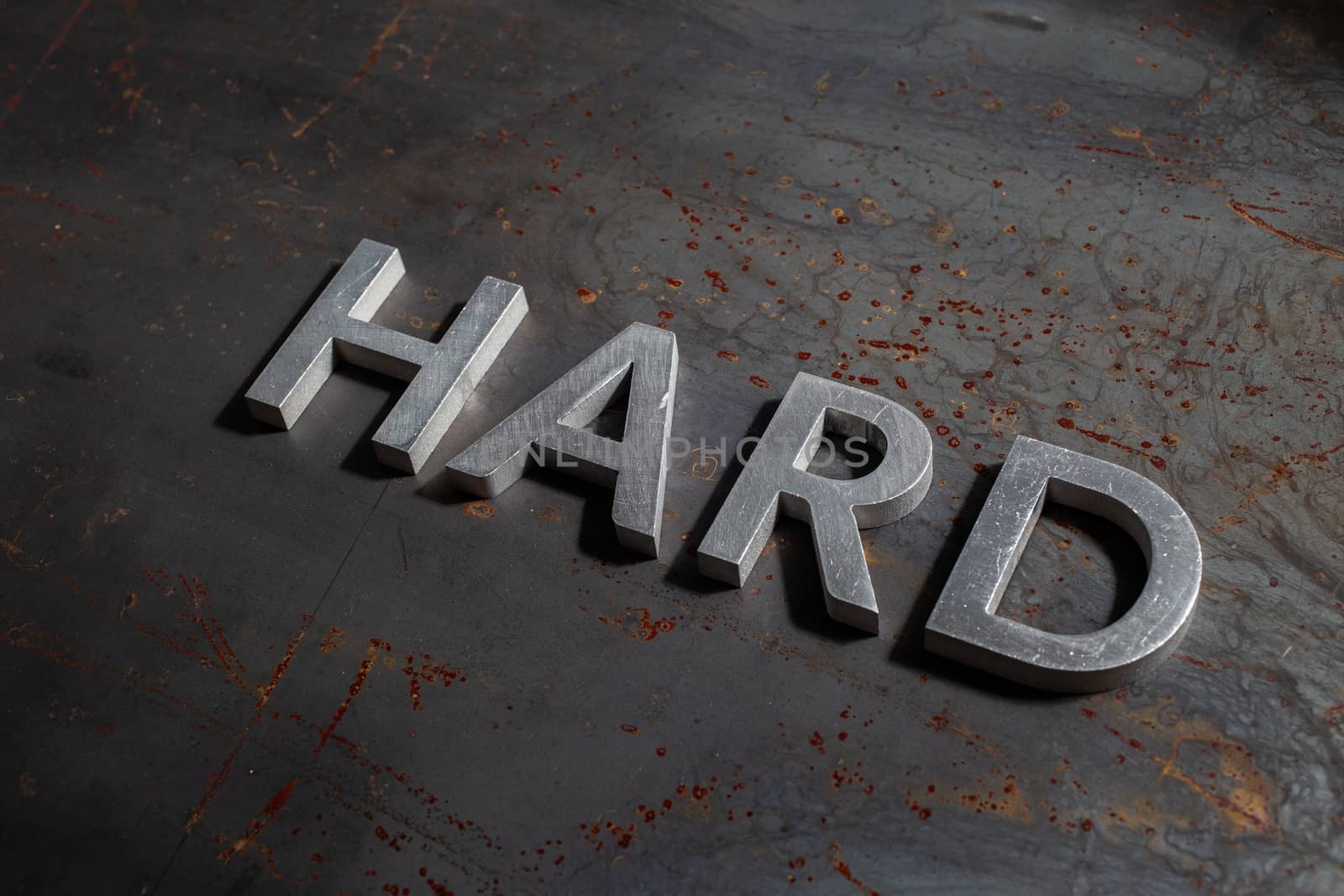 the word hard laid with silver metal letters on rusted burnt iron flat surface background in descending diagonal composition