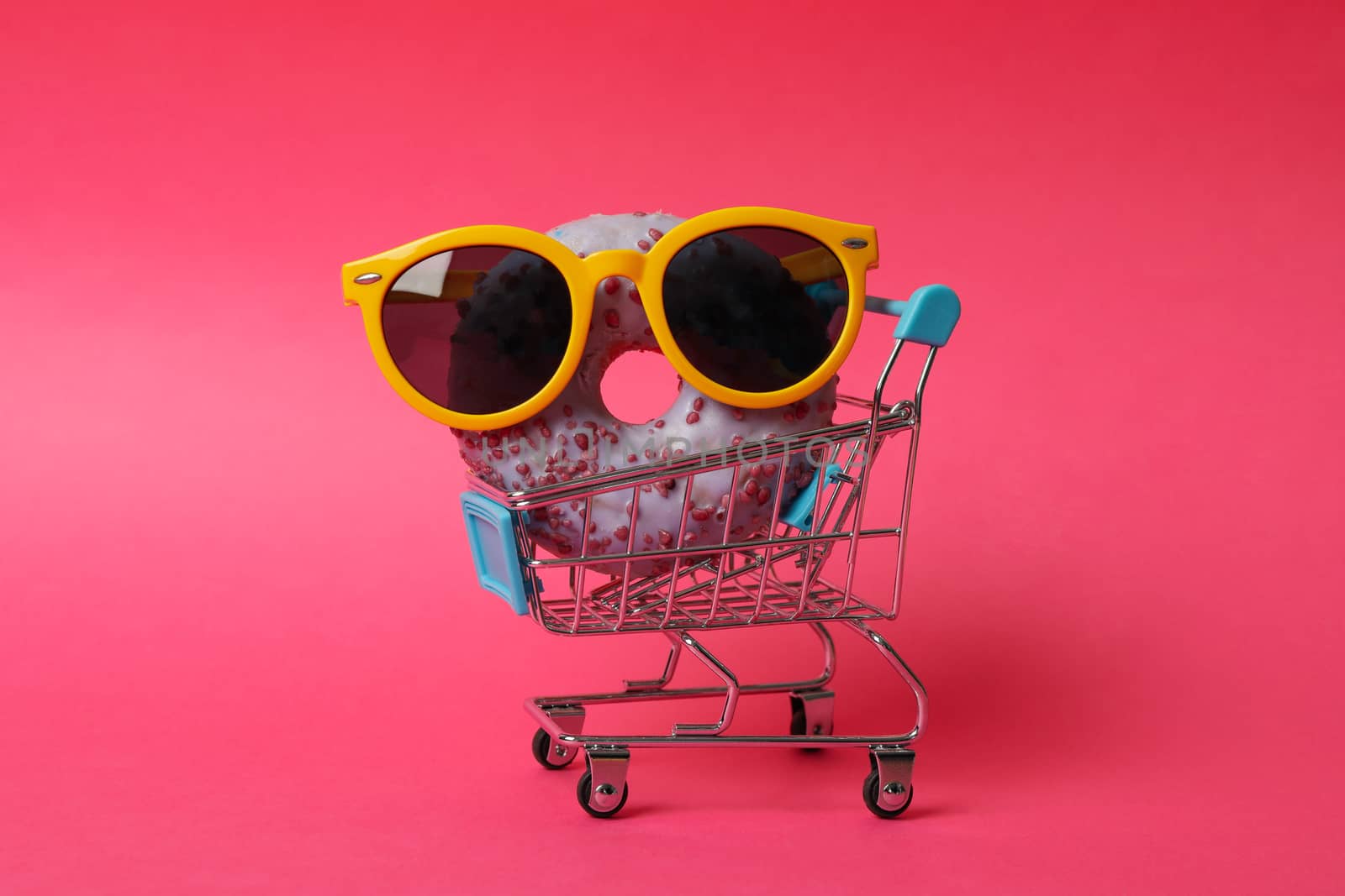 Shop trolley with sunglasses and donut on pink background