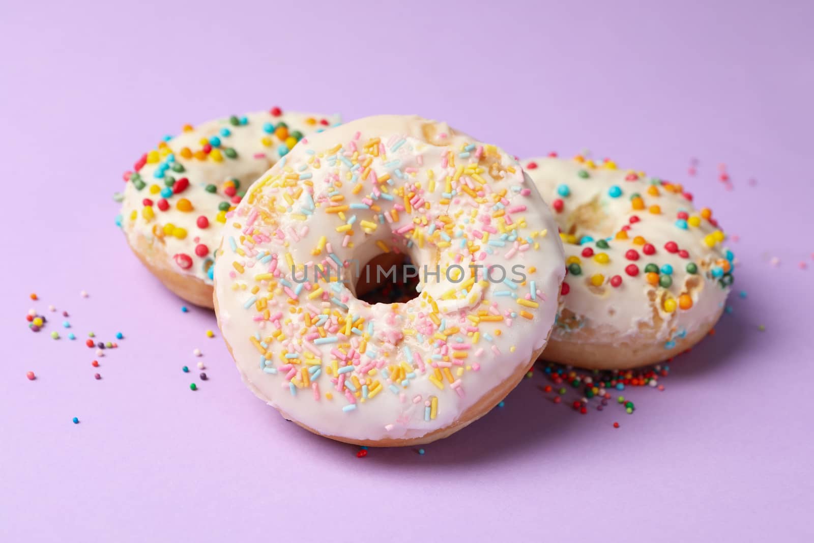 Three tasty donuts on violet background, close up