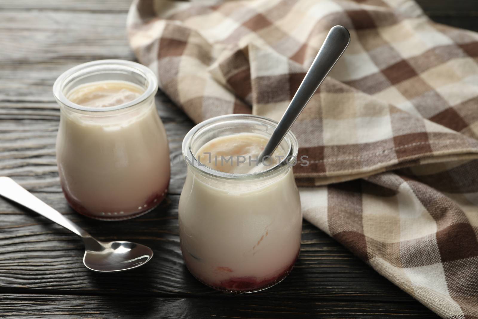 Glass jars of yogurt, spoons and napkin on wooden background