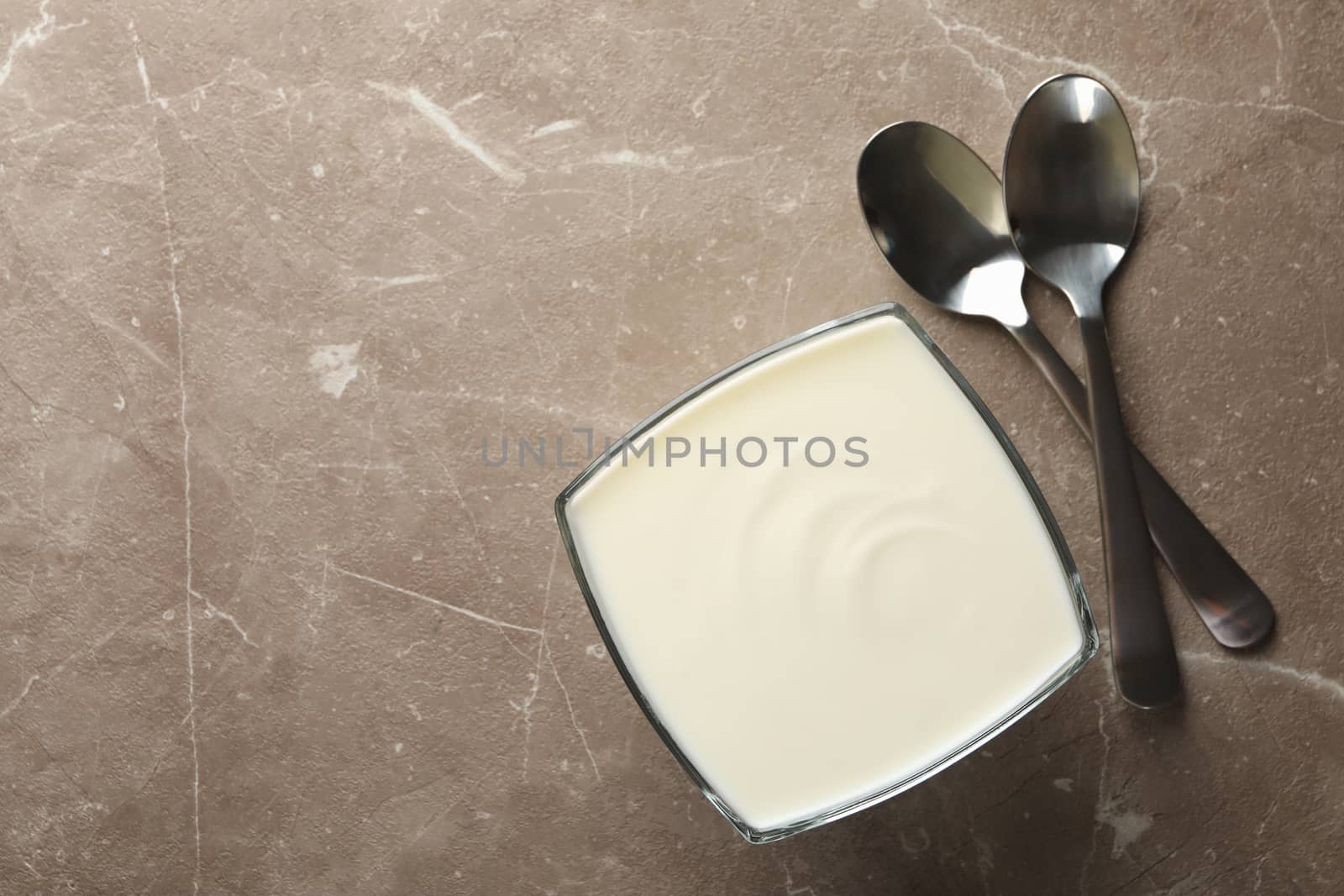 Spoons and bowl of sour cream on gray background, top view