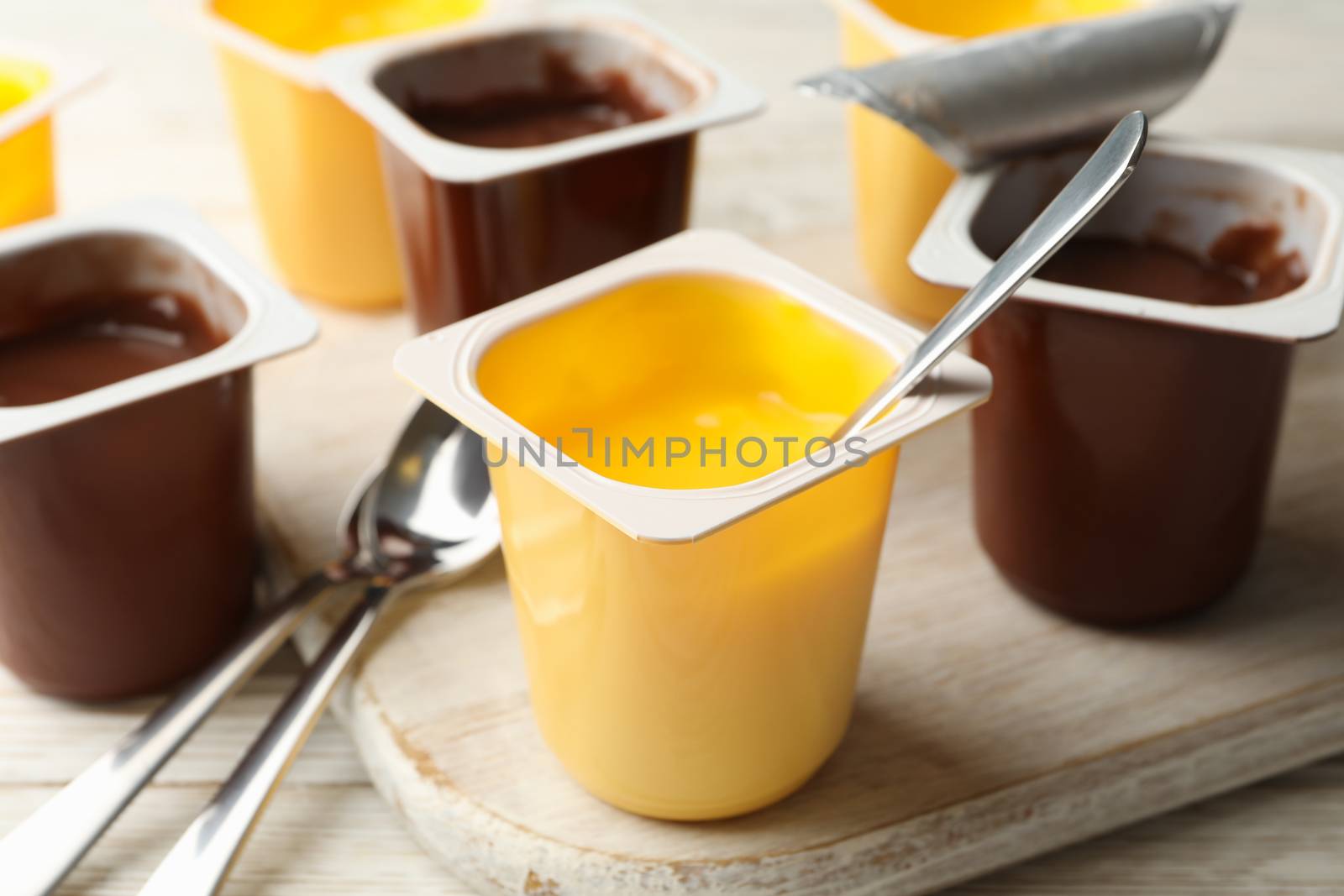 Board with plastic cups of yogurt and spoons on gray background