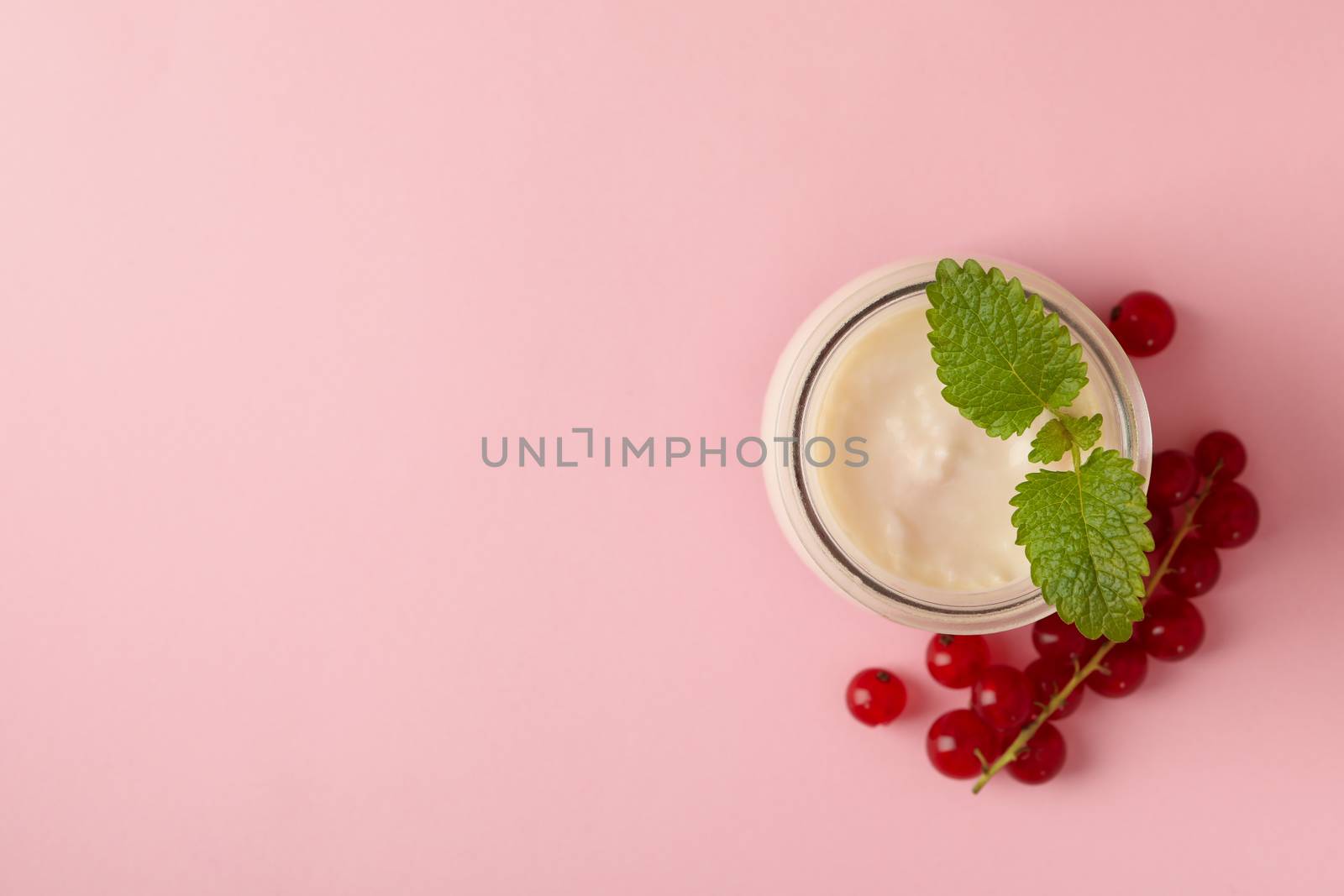 Glass jar of sour cream yogurt and cranberry on pink background