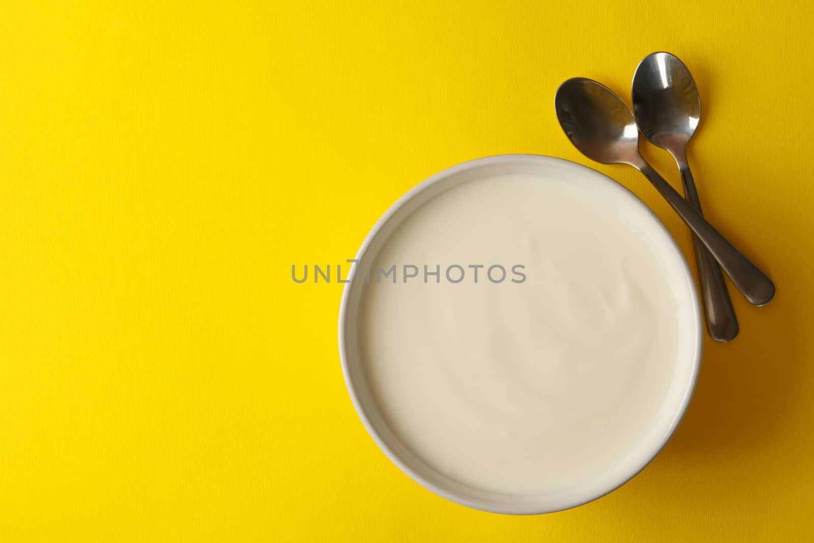 Bowl of sour cream yogurt and spoons on yellow background