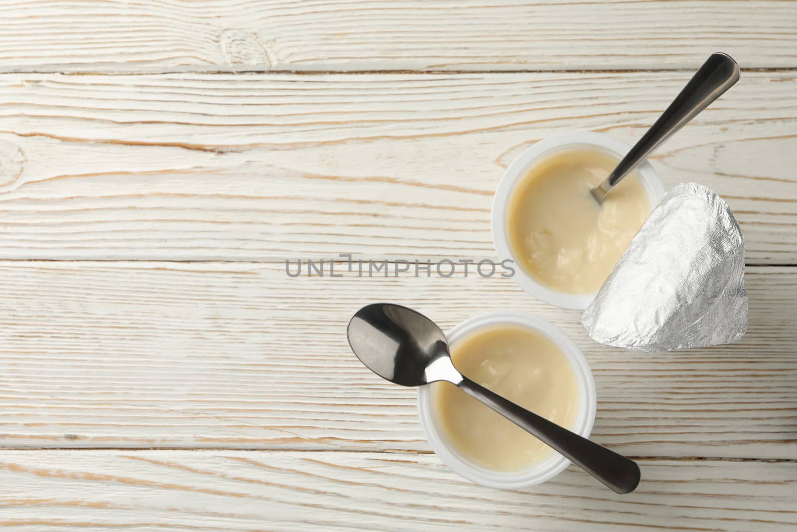 Plastic cups of yogurt and spoons on white wooden background