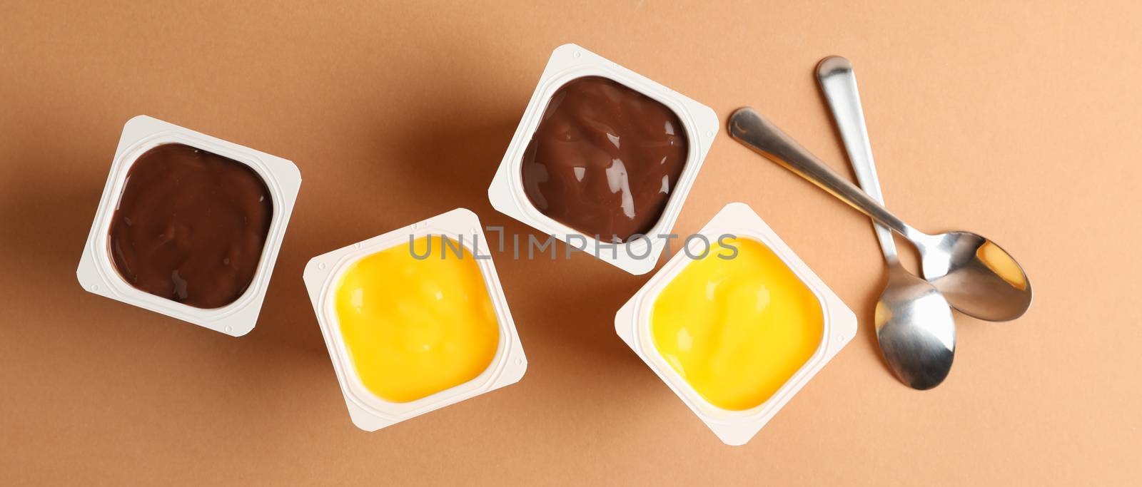 Plastics cups of yogurt on brown background, top view