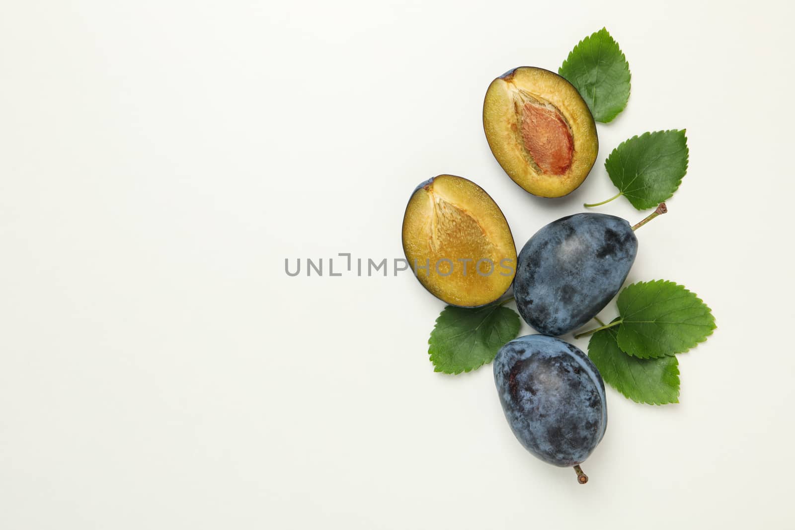 Fresh plums and leaves on white background, top view