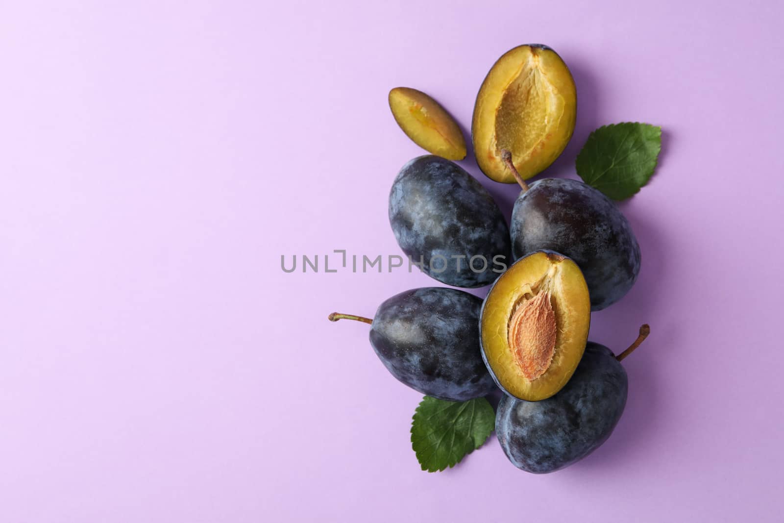 Fresh plums and leaves on violet background, top view