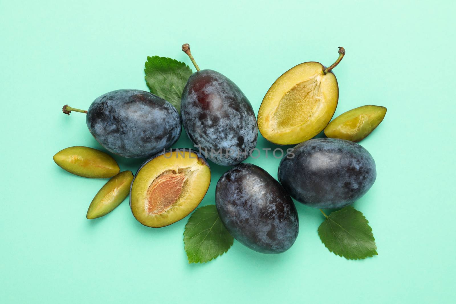 Fresh plums and leaves on mint background, top view