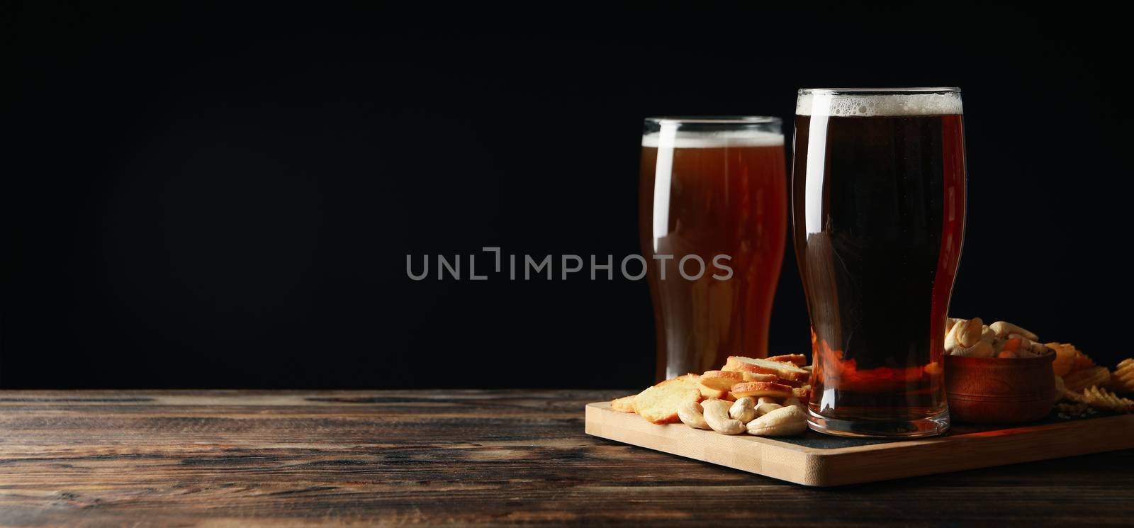 Glasses of beer and snacks on wooden table