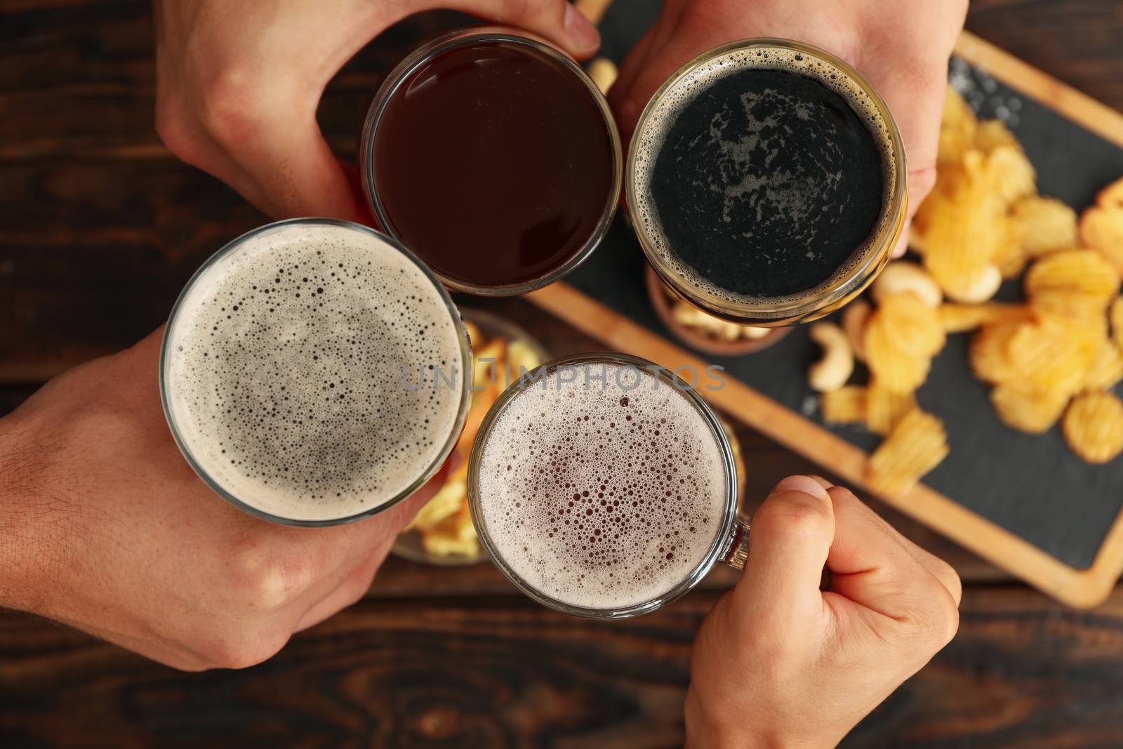 Four men cheers with beer on wooden background with snacks